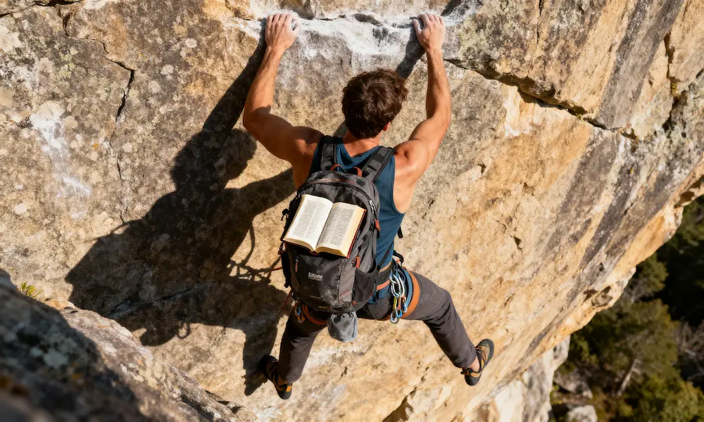 Determined rock climber scales challenging face with open Bible in backpack and dramatic afternoon light.