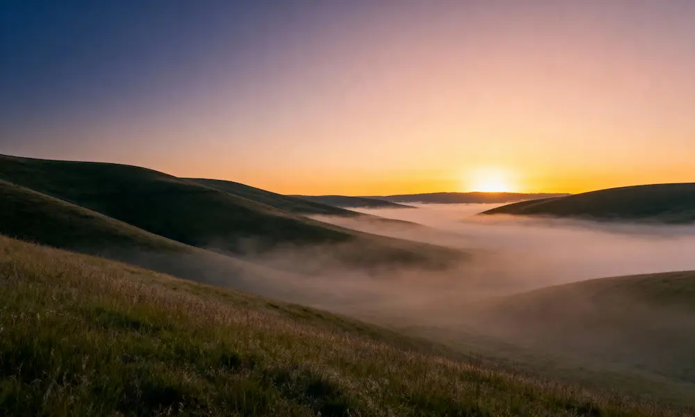 First light of dawn over rolling hills with soft mist, symbolizing breakthrough and new beginnings