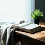 Open Bible near a bright window with plant and blanket, ample copy space.